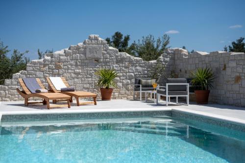 una piscina con due sedie a sdraio accanto a un muro di pietra di Villa Mista a Sutivan (San Giovanni di Brazza)