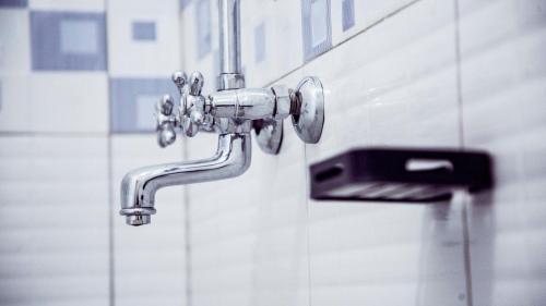 a chrome bathroom faucet on a white wall at Stusky Lark Mini Hotel Seeta in Seeta