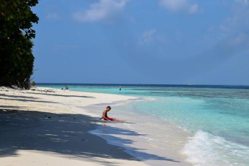 a person sitting on a beach in the water at Island Grand Maldives in Hangnaameedhoo
