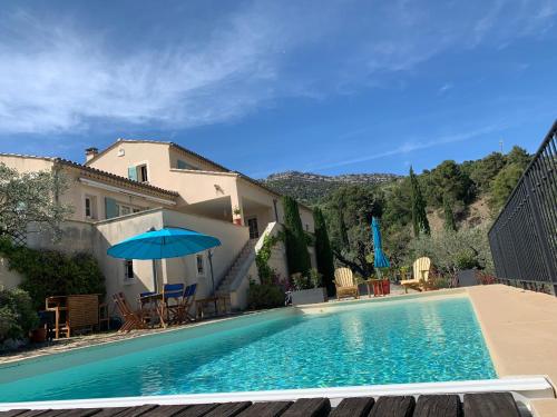 a swimming pool with a blue umbrella and chairs at Mas Christine in Buis-les-Baronnies
