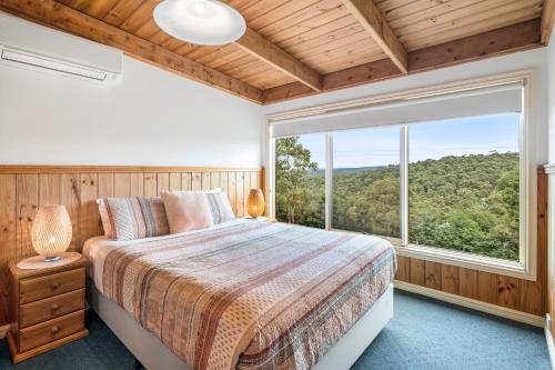 um quarto com uma cama e uma grande janela em Lorne Bush House Cottages & Eco Retreats em Lorne