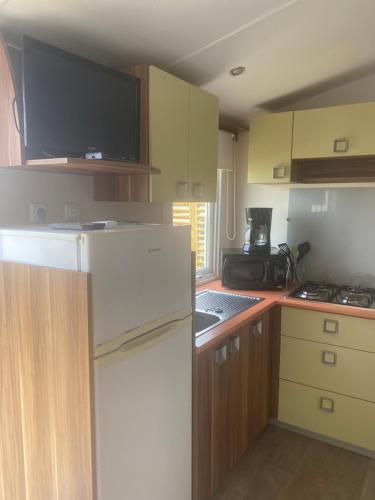 La cuisine est équipée d'un réfrigérateur blanc et de placards en bois. dans l'établissement CAMPING LE PHARE D OPALE mobile home L07, à Le Portel