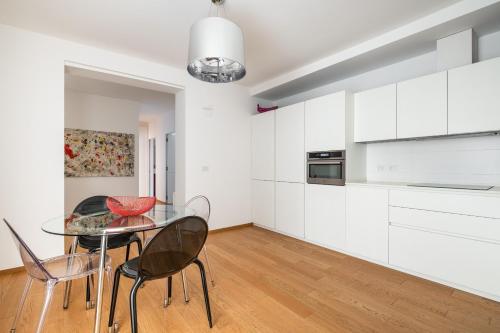 ボローニャにあるSanto Stefano Design Apartment by Wonderful Italyの白いキャビネット、ガラスのテーブルと椅子付きのキッチンが備わります。