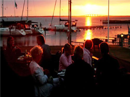 a group of people sitting at a bar watching the sunset at Talluddens Stugby in Färjestaden