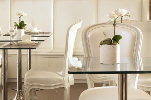 a dining room with white chairs and a glass table with a plant at Hôtel Caron le Marais in Paris