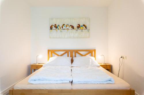 uma cama com lençóis brancos e uma imagem de pássaros em Ferienwohnpark Immenstaad am Bodensee Zwei-Zimmer-Apartment 49 19 em Immenstaad am Bodensee