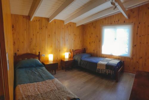 a bedroom with two beds and a window and wooden walls at CABAÑA LA SUREÑA in San Martín de los Andes