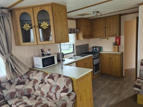 a kitchen with wooden cabinets and a couch in a caravan at 4 Berth Golden Sands Ingoldmells (Siesta) in Ingoldmells