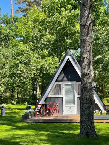 a small house with a porch and red chairs in a yard at Camping Milk in Usmenieki