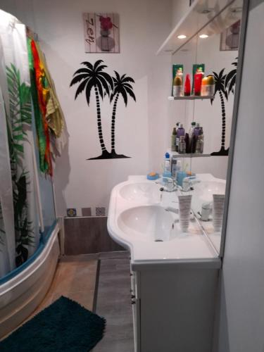 La salle de bains est pourvue d'un lavabo et de palmiers sur le mur. dans l'établissement Maison LUCIA, à Saint-Pierre