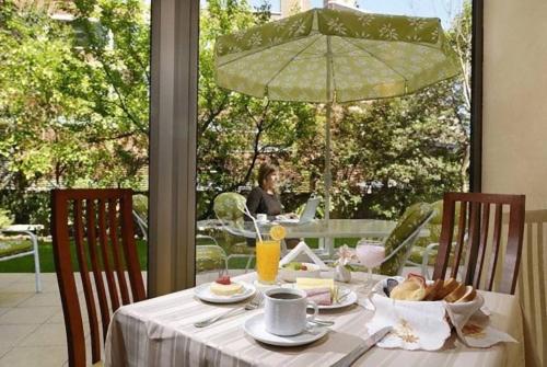 a table with food and a woman sitting at a table with an umbrella at Hotel Eurotel El Bosque in Santiago