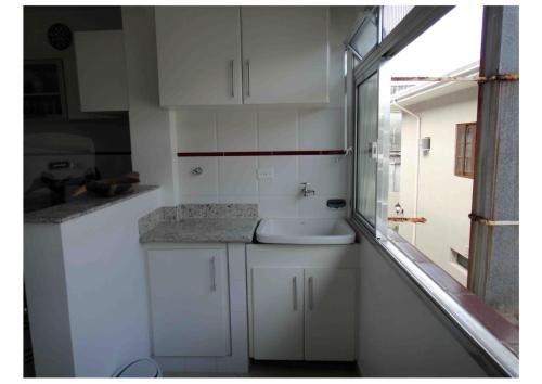une cuisine blanche avec un évier et une fenêtre dans l'établissement Guarujá, apartamento a 100 metros da praia da enseada., à Guarujá