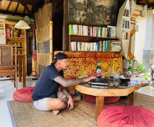 a woman sitting on the floor in front of a laptop at Bale Bali House in Ubud