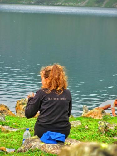 a woman sitting on a rock by a body of water at Kashmir Outlook Adventures in Pahalgām