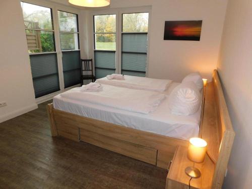 a large bed in a room with two windows at Darßer Strandgut - Haus Ahrenshooper Holz in Ahrenshoop