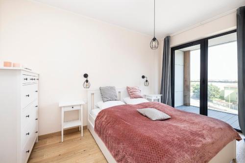 a white bedroom with a large bed with a red blanket at Apartament 409 Natural Darłówko in Darłowo