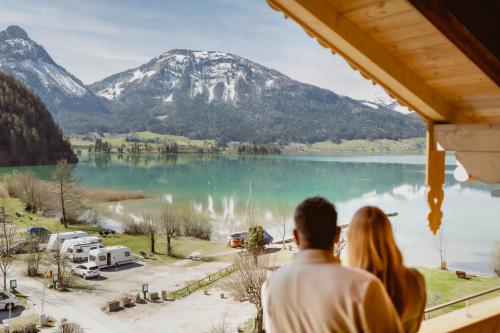 Una pareja mirando por una ventana a un lago y montañas en Seehotel Berau, en St. Wolfgang