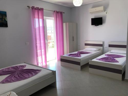 two beds in a room with pink curtains at GB Rooms in Ksamil