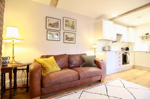a brown leather couch in a living room with a kitchen at 14th century Rose cottage, Centre of Alfriston By Air Premier in Alfriston