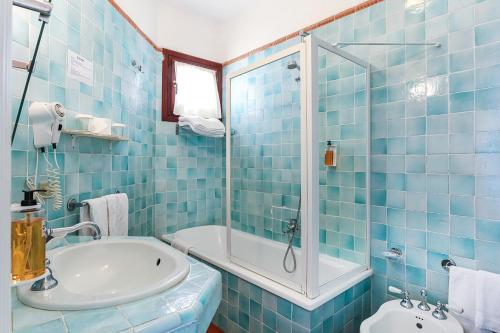 a blue tiled bathroom with a tub and a sink at Hotel Stefania Boutique Hotel by the Beach in Olbia