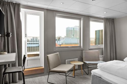 a hotel room with a bed and chairs and windows at Comfort Hotel Børsparken in Oslo