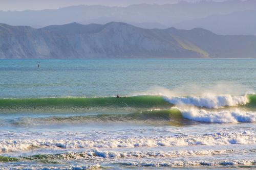 a surfer riding a wave in the ocean at Whispering Sands Beachfront Motel in Gisborne