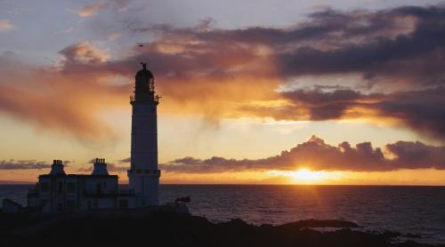 a lighthouse with the sunset in the background at Corsewall Lighthouse Hotel in Kirkcolm