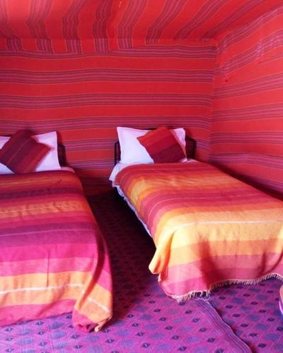 two beds in a room with red and yellow stripes at Overnight Desert Camp in Merzouga