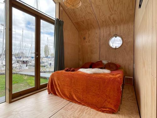 a bedroom with a bed with an orange blanket and a window at Wikkelhuis 31- Pet Friendly in Stavoren