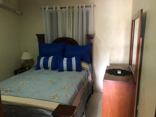 Un dormitorio con una cama con almohadas azules y una mesa. en Apartamentos Kika en San Felipe de Puerto Plata