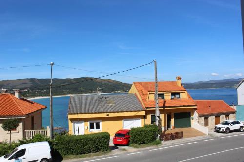 a yellow house with red roofs and cars parked on a street at Piso amplio con vistas al mar y playa a 50 mts in Fisterra
