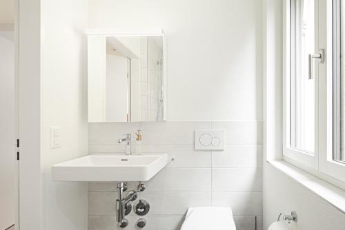 a white bathroom with a sink and a mirror at Mühlensteg Apartments by VISIMO - Elegant, Quiet, Central in St. Gallen