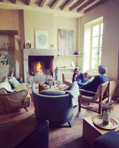 two people sitting in a living room with a fireplace at Maison d'hôtes La Doucelle culture et bien-être in Lignieres-Orgeres