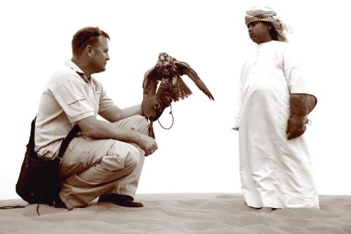 a man holding a bird and a woman in the sand at Bedouin Oasis Desert Camp- Ras Al Khaimah in Ras al Khaimah