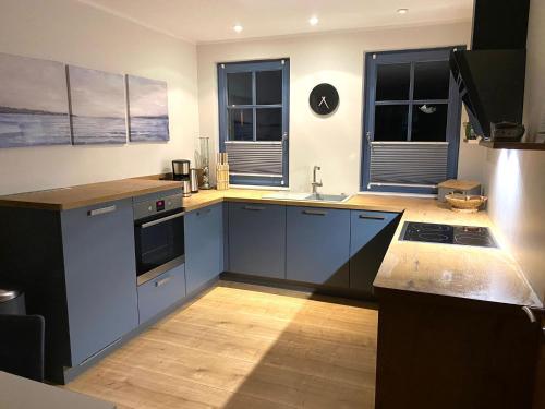 cocina con armarios azules y fregadero y 2 ventanas en Ferienwohnung Born am Darßwald EG, en Born