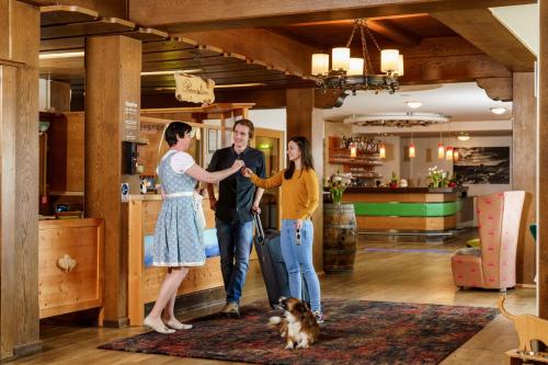 Drei Leute, die mit einem Hund Händchen schütteln. in der Unterkunft Almfrieden Hotel & Romantikchalet in Ramsau am Dachstein