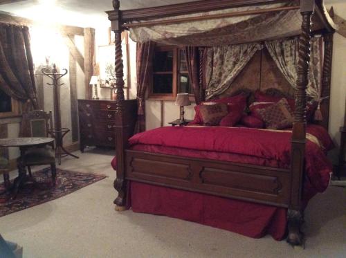 a bedroom with a canopy bed with red sheets and pillows at Valley Farmhouse, Westhall in Southwold