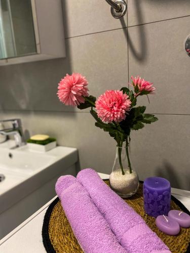 a bathroom with a vase of pink flowers and purple towels at Apartman Barocco in Trebinje