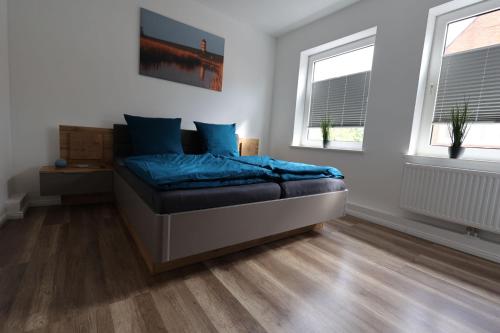 a bedroom with a bed with blue sheets and two windows at Kajüte 19 in Emden