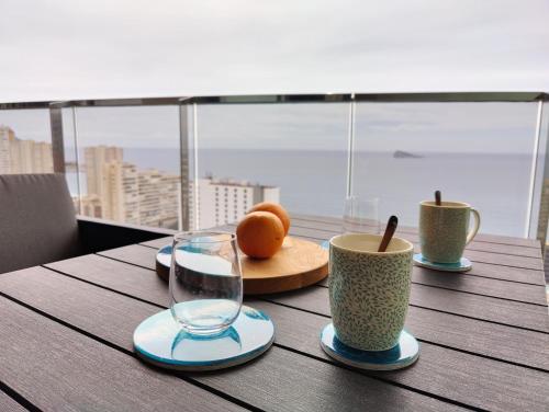 een houten tafel met twee kopjes en sinaasappels erop bij SUNSET WAVES sea & sky apartment in Benidorm