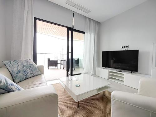 a white living room with a white couch and a tv at SUNSET WAVES sea & sky apartment in Benidorm