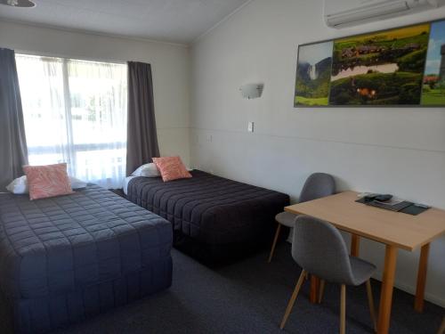Cette chambre comprend deux lits, un bureau et une table. dans l'établissement Tower Road Motel, à Matamata