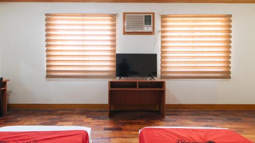 a room with two beds and a television and windows at RedDoorz Premium @ Nick Hotel Gerona Tarlac in Tarlac