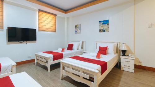 two beds in a white room with a flat screen tv at RedDoorz Premium @ Nick Hotel Gerona Tarlac in Tarlac