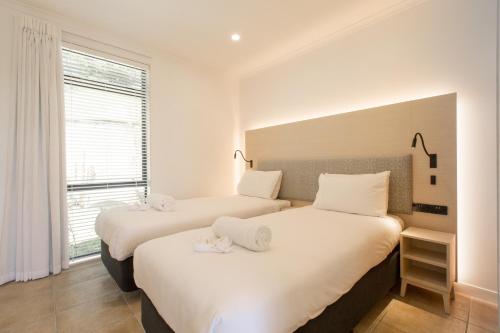 two beds in a room with white walls and a window at Waiheke Island Resort Conference & Accomodation Centre in Ostend