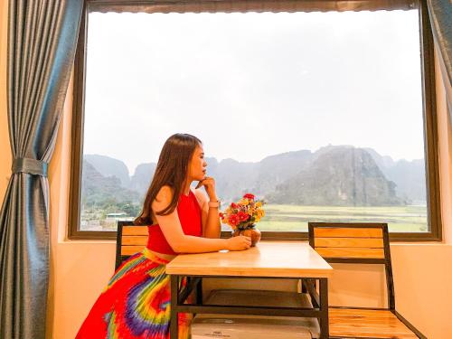 a woman sitting at a table with flowers in front of a window at Cherry homestay in Ninh Binh