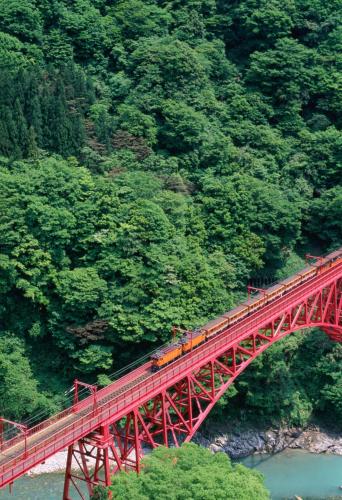 a train on a red bridge over a river at Entaijiso in Kurobe