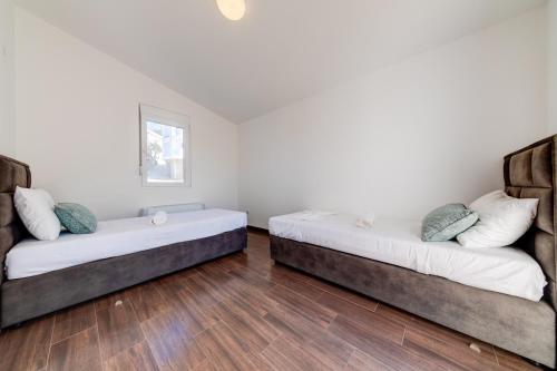 two beds in a room with white walls and wooden floors at Dolaca Villas in Sutomore