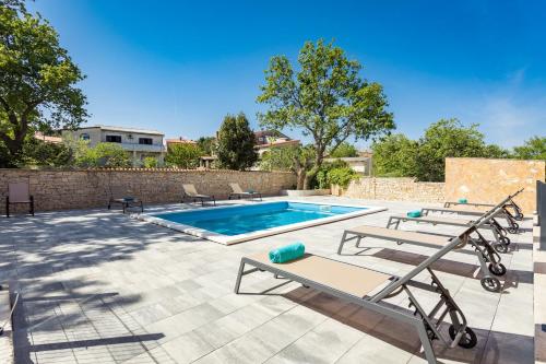 uma piscina com duas espreguiçadeiras ao lado de uma parede de tijolos em Apartments Cesare with Shared Pool em Ližnjan