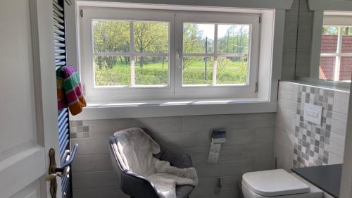 a bathroom with a chair and a toilet and two windows at Ferienhaus Spreewald direkt am Wasser in Burg Kauper